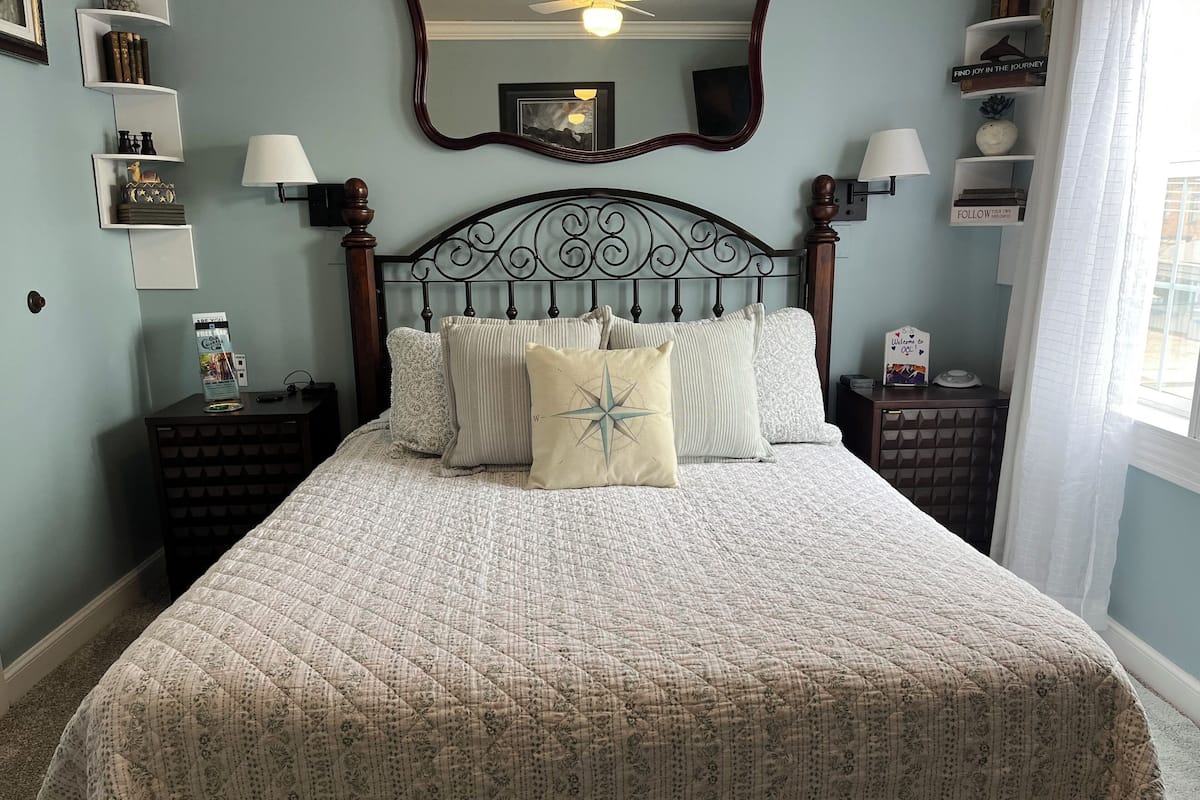 A neatly made bed with a quilted cover and multiple pillows, flanked by nightstands with lamps and decorative items.