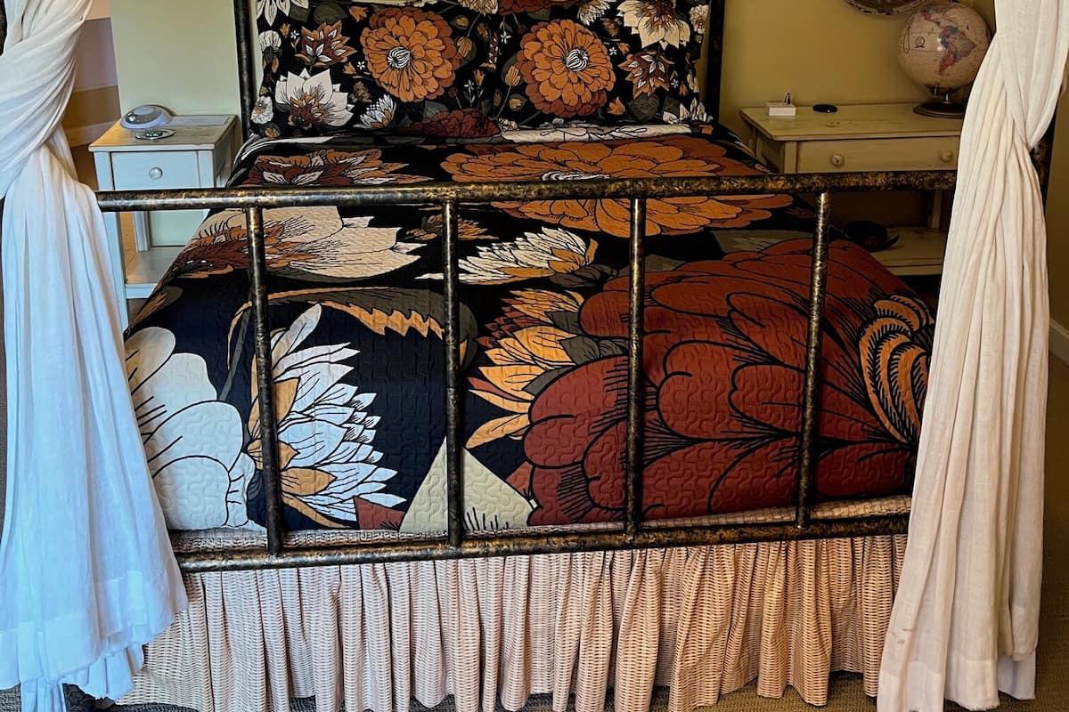 A four-poster bed with a floral bedspread, a globe, and a wall-mounted lamp.