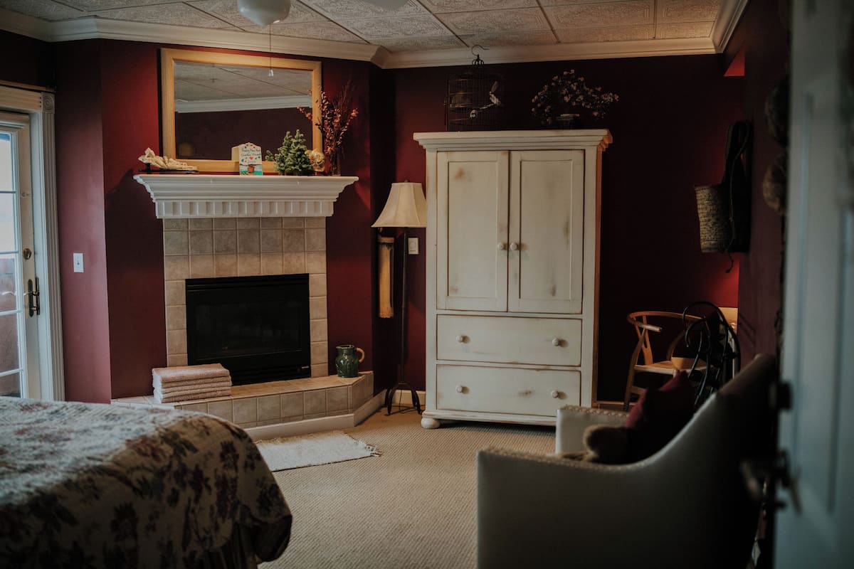 A room with a fireplace, a white cabinet, a chair, and a bed with a floral bedspread.