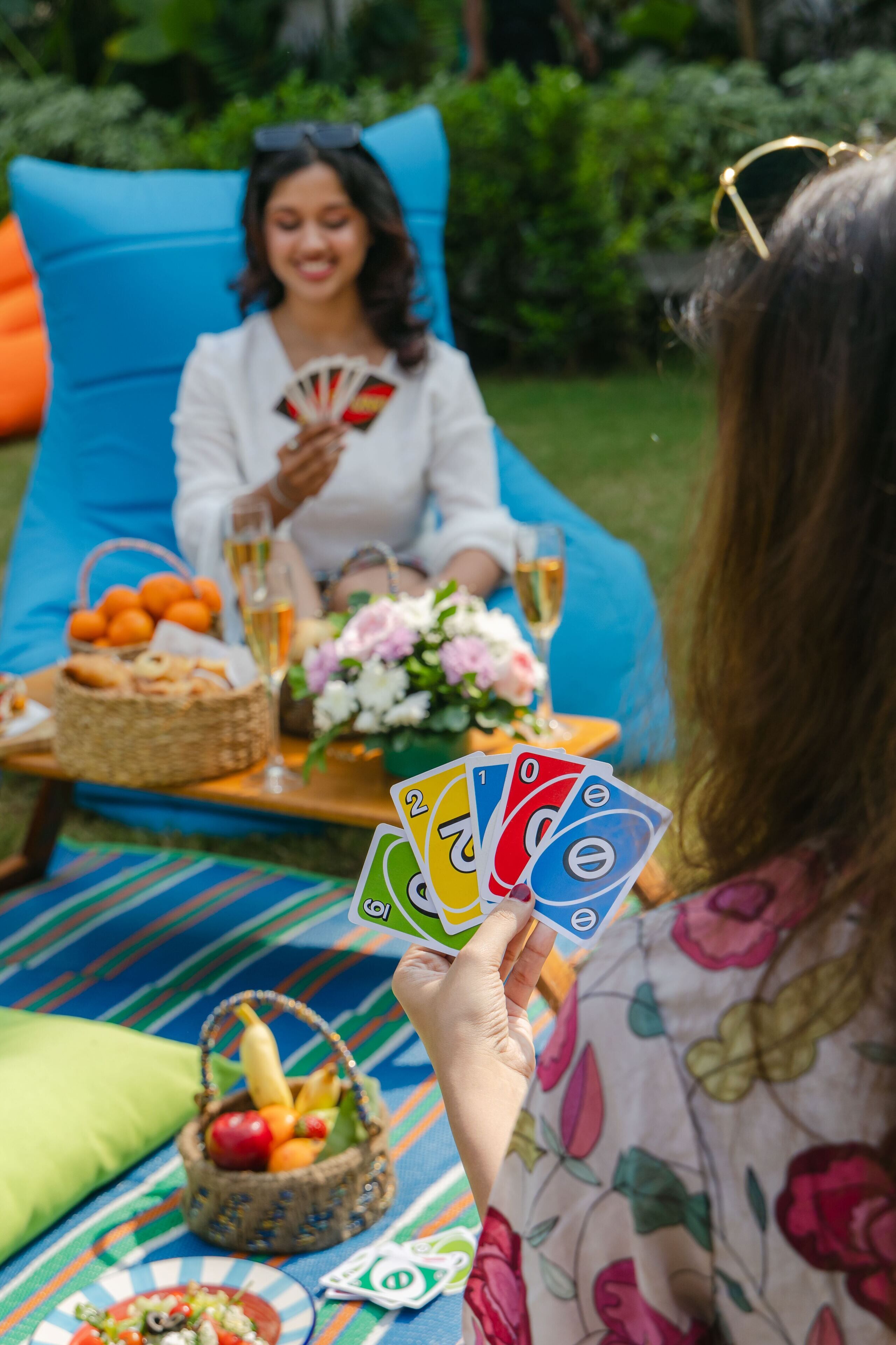 A picnic setup with a basket of fruits and vegetables, a plate of food, and a fan of playing cards.