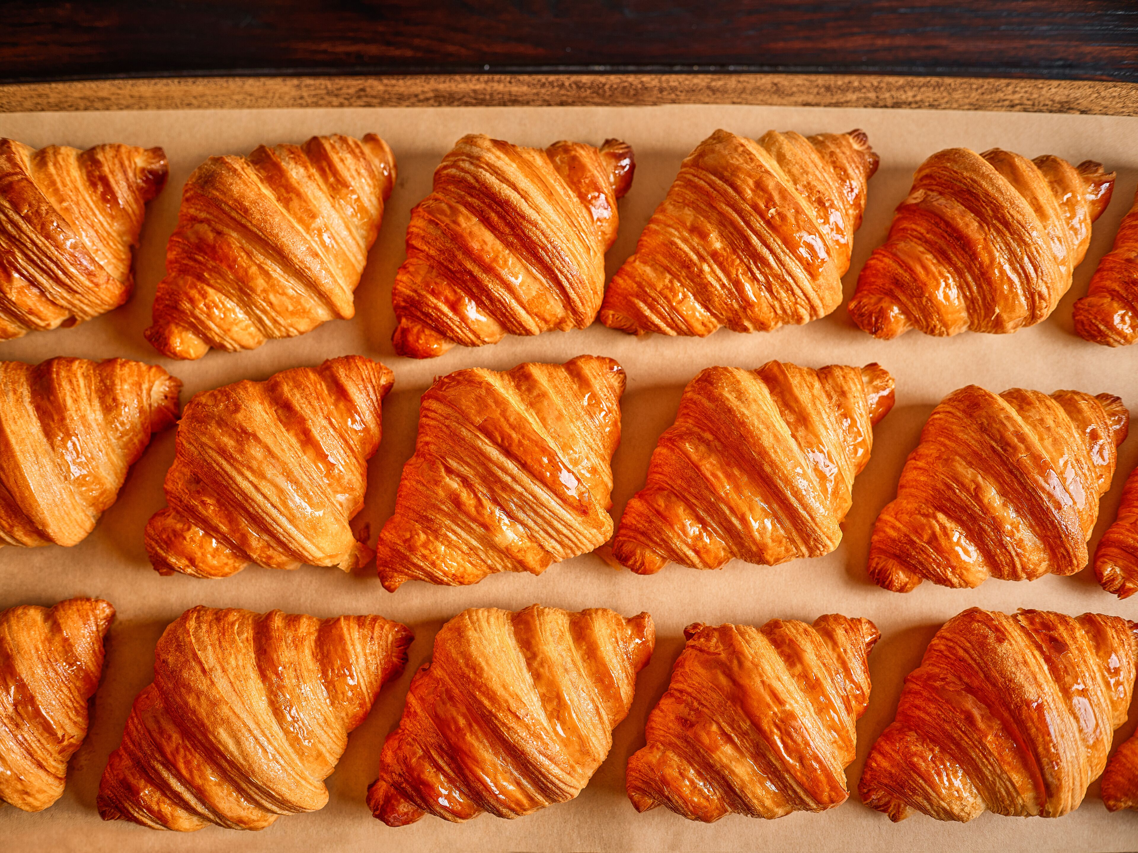 A tray of golden-brown croissants arranged neatly on parchment paper.