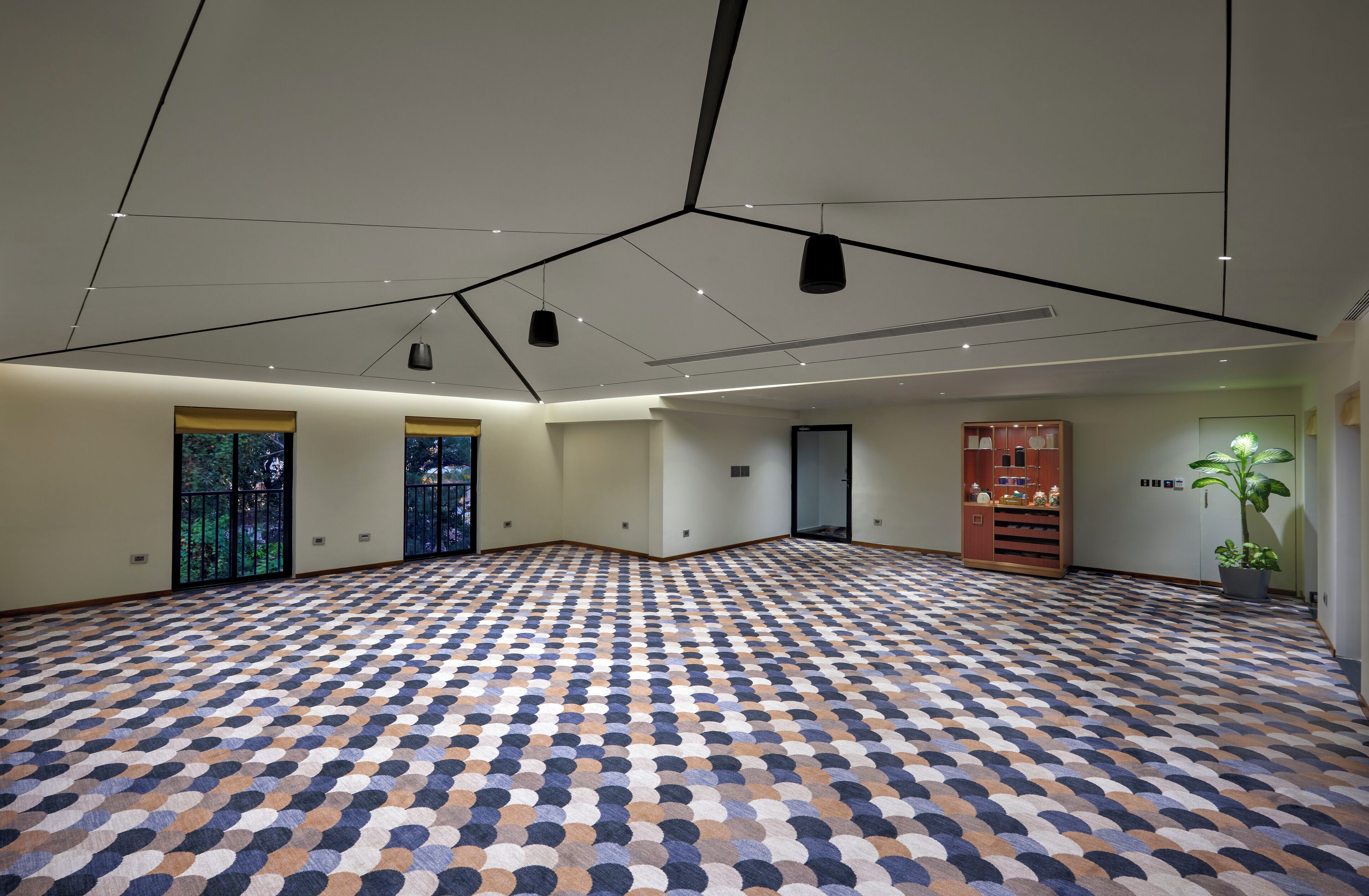 A spacious room with a patterned floor, large windows, and a ceiling with hanging lights.