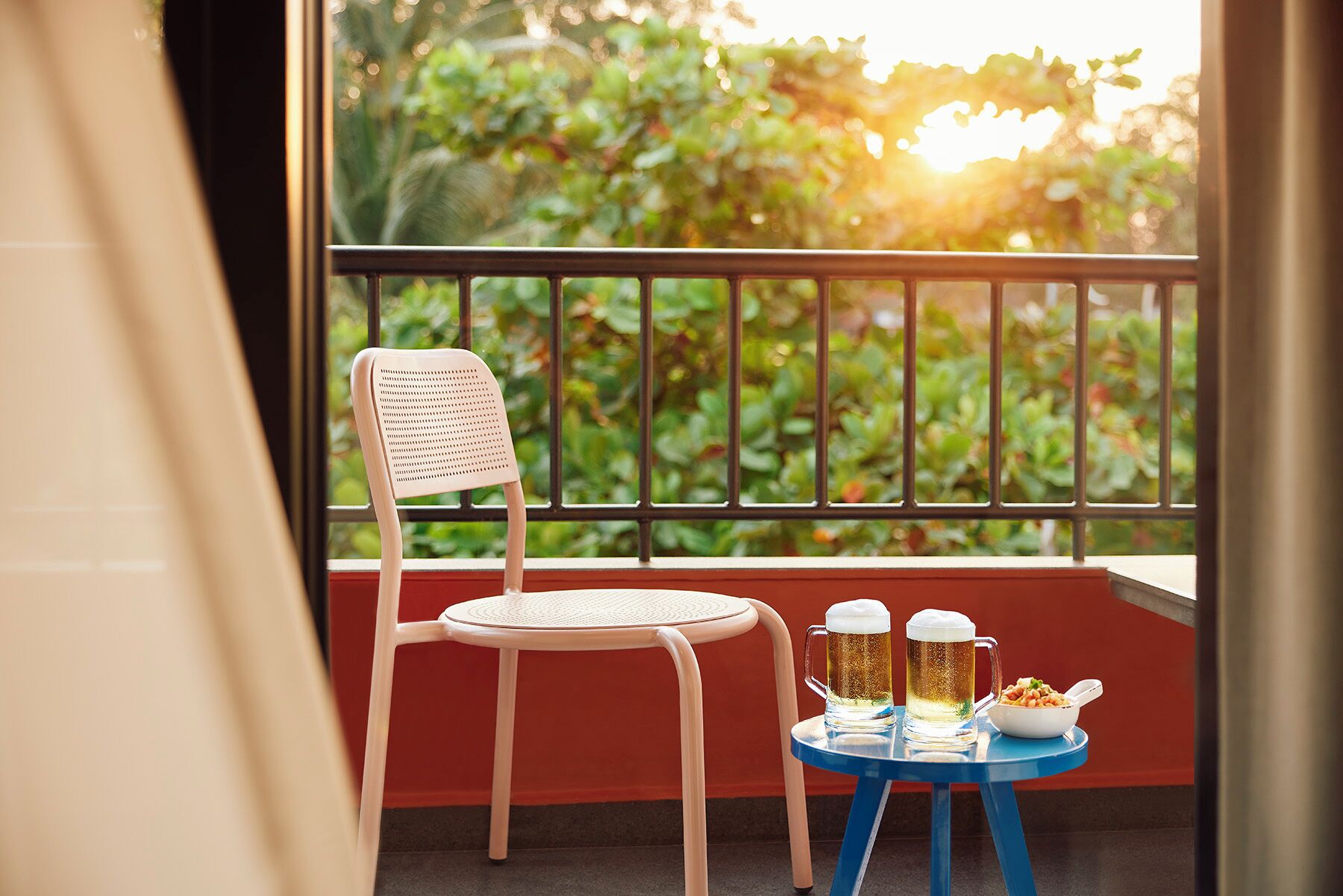 A balcony with a wicker chair and a small table holding a beer mug and a bowl of snacks.