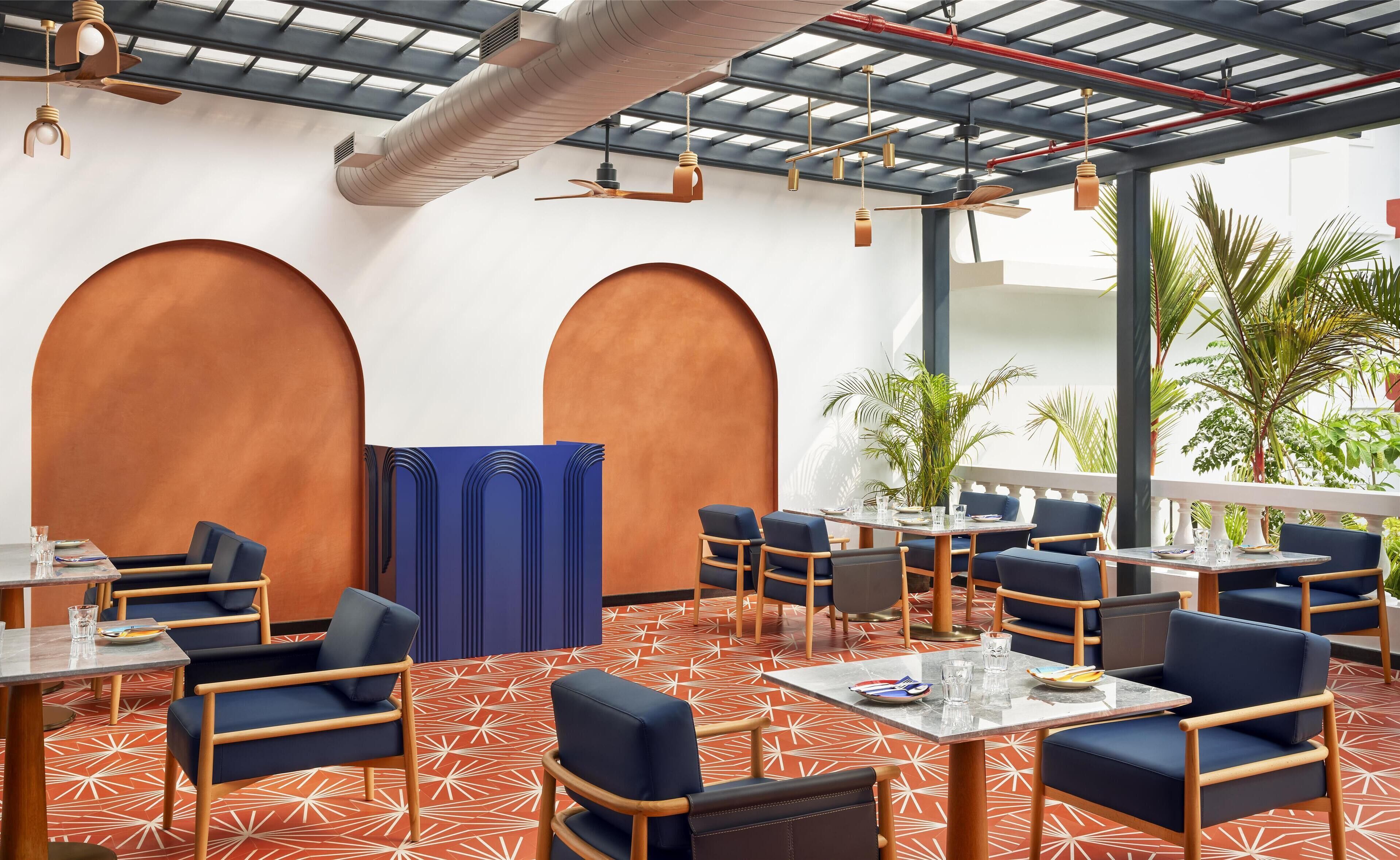 A modern indoor seating area with tables and chairs, large arched wall features, and ceiling fans.