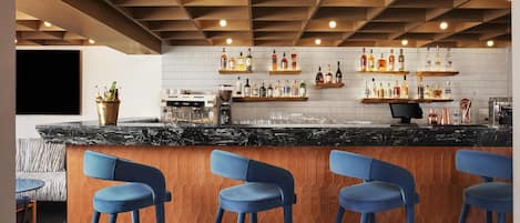 Zona de bar con encimera de mármol negro, taburetes azules y estantes llenos de botellas de licores.