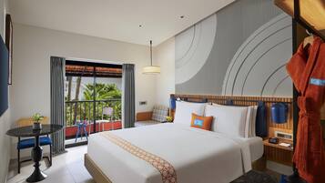 A hotel room with a large bed, a bedside table, a chair, a small table, and a view of greenery outside.