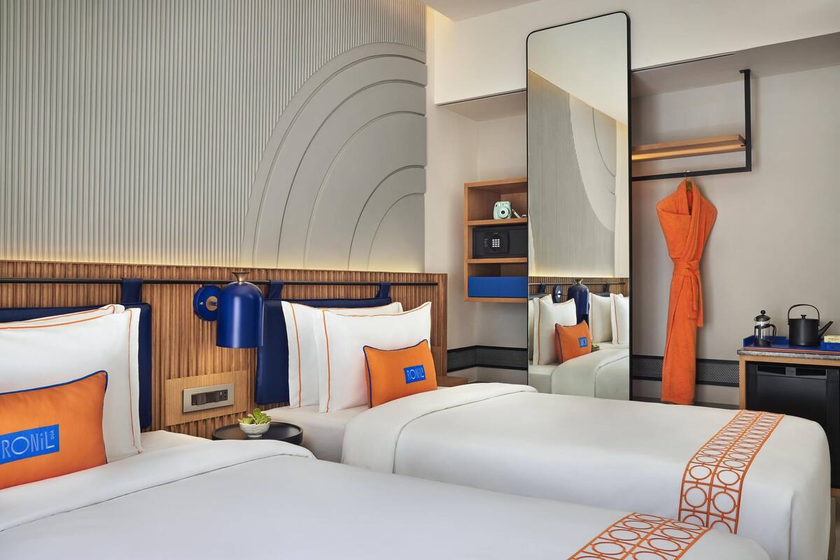 Une chambre d’hôtel avec deux lits, un grand miroir, une armoire et une petite table avec une bouilloire.