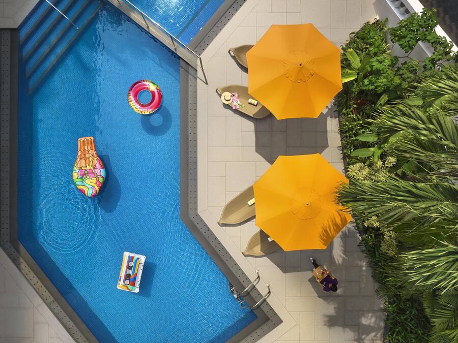 Vista aérea de una piscina con un flotador colorido, una sombrilla y una persona con una bandeja.
