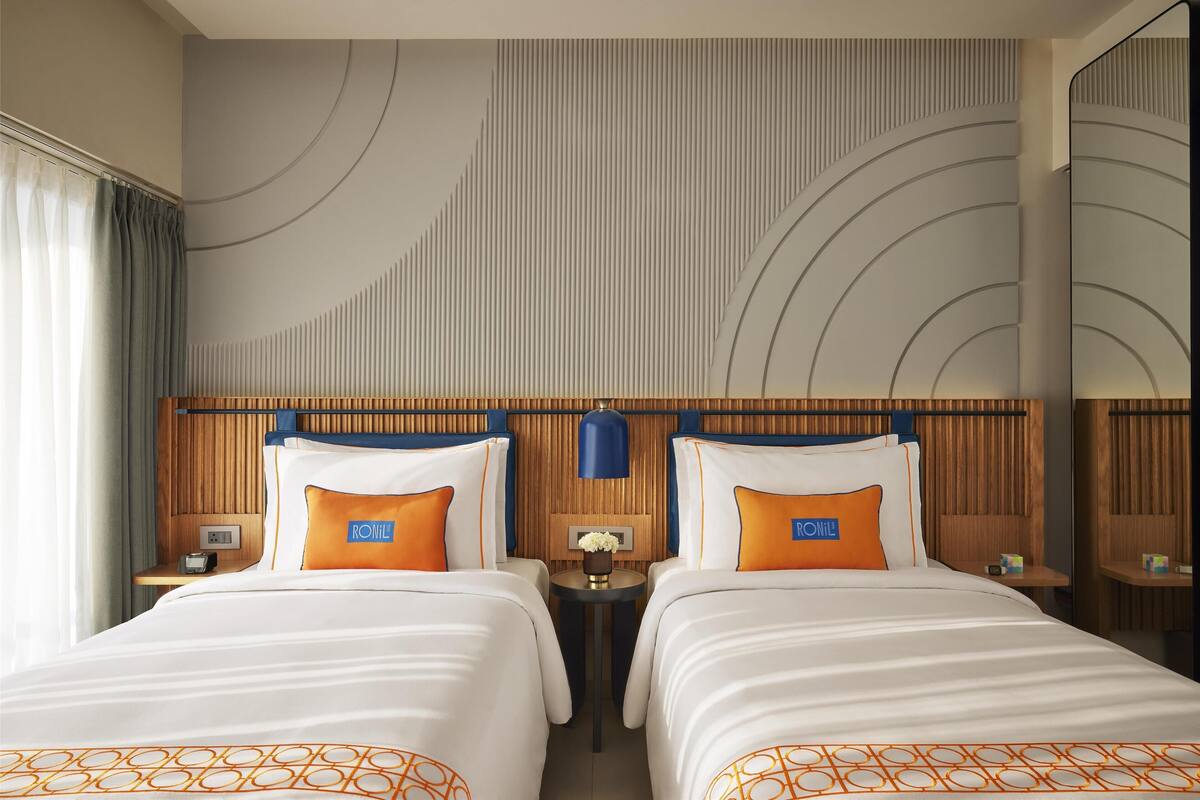 Une chambre d’hôtel avec deux lits, une tête de lit en bois, un miroir et un mur orné d’un motif circulaire.
