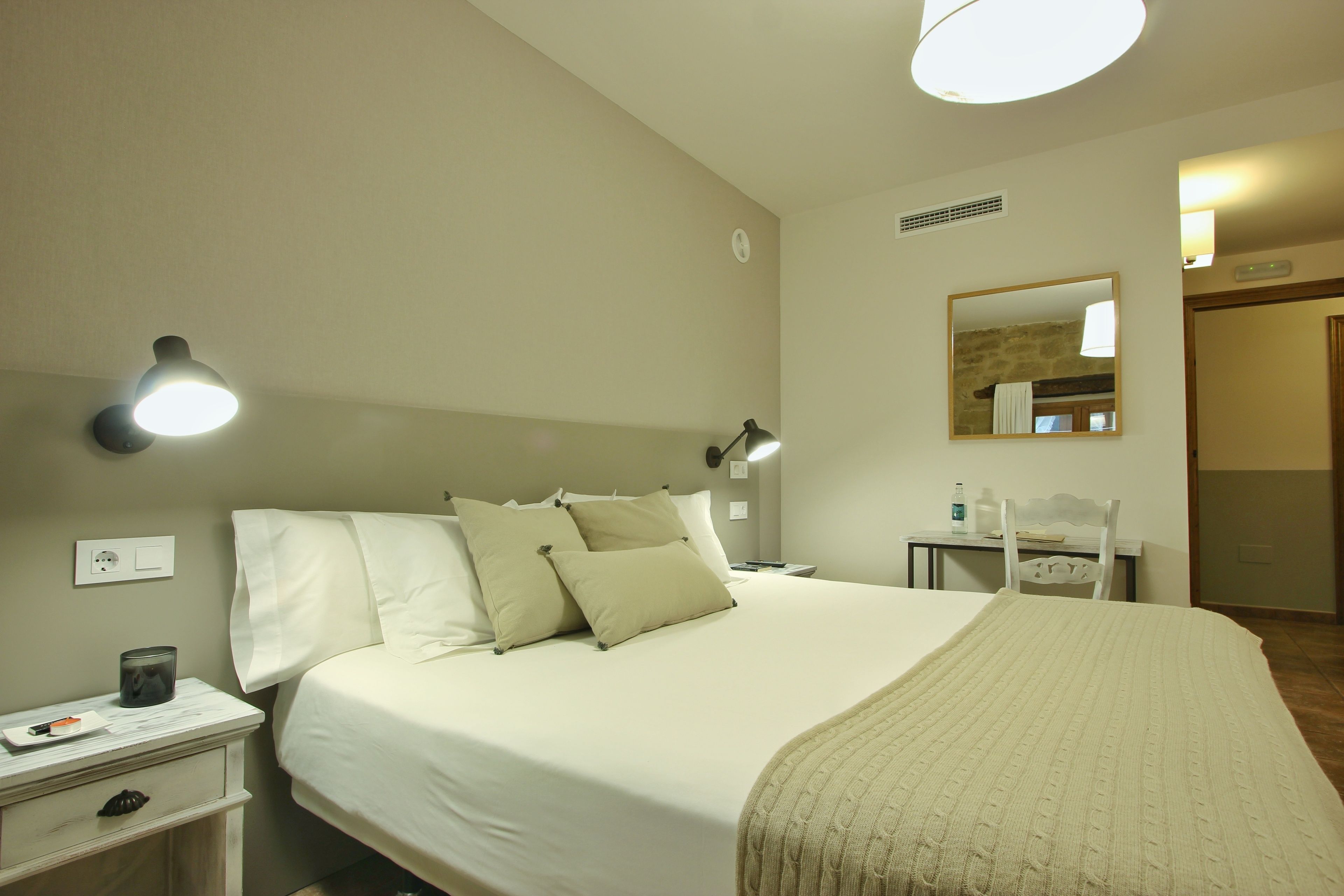 A hotel room with a bed, bedside table, lamp, and a mirror on the wall.