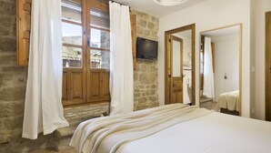 Un dormitorio con pared de piedra, puertas de madera, una cama con cubrecama blanco y un televisor montado en la pared.