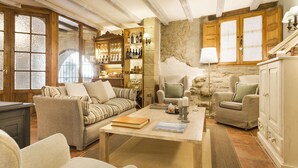 Una sala de estar acogedora con un sofá, sillones, una mesa de centro y una estantería llena de libros y botellas.