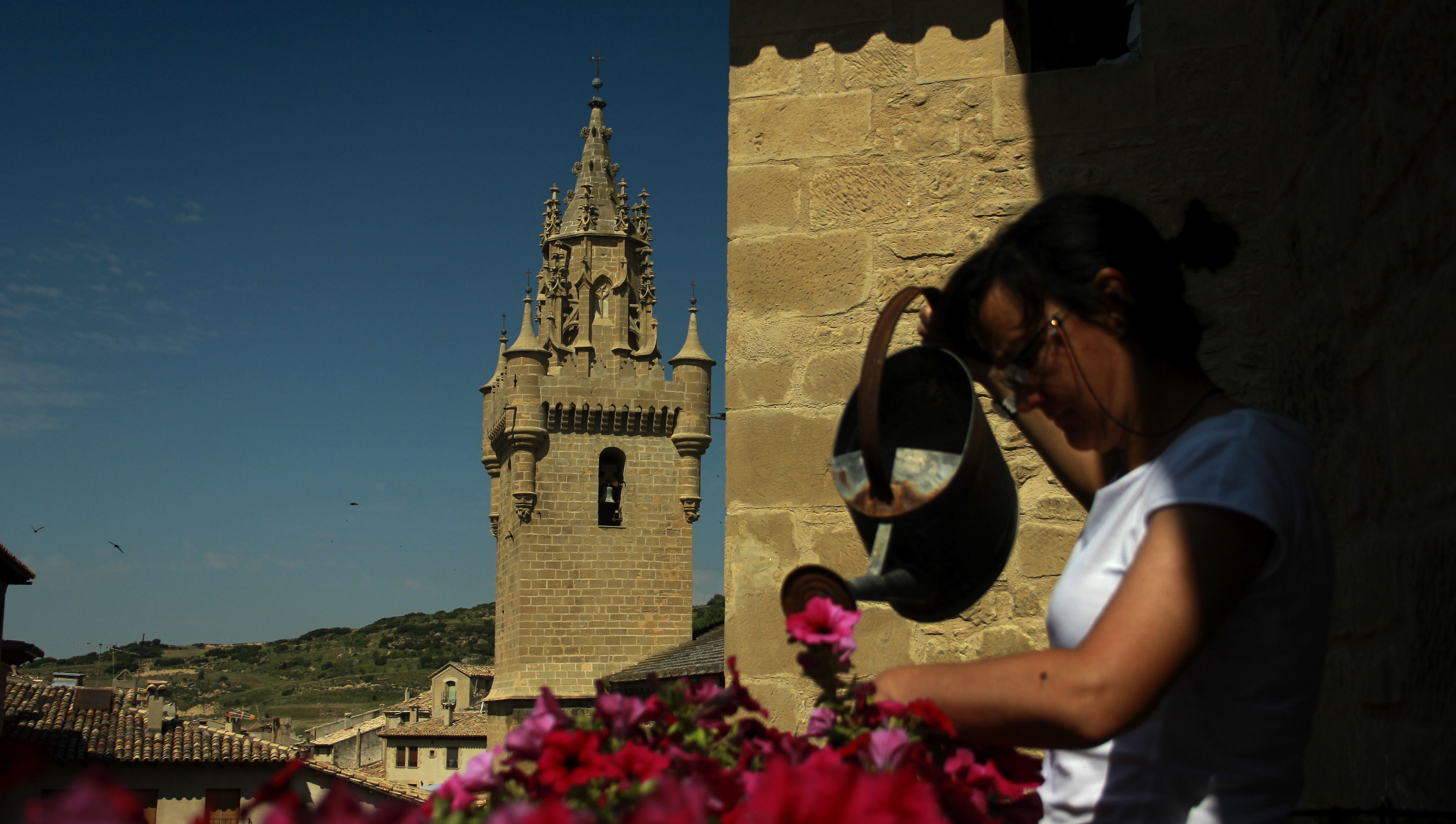 A historic tower with a bell tower and a person pouring water on flowers.