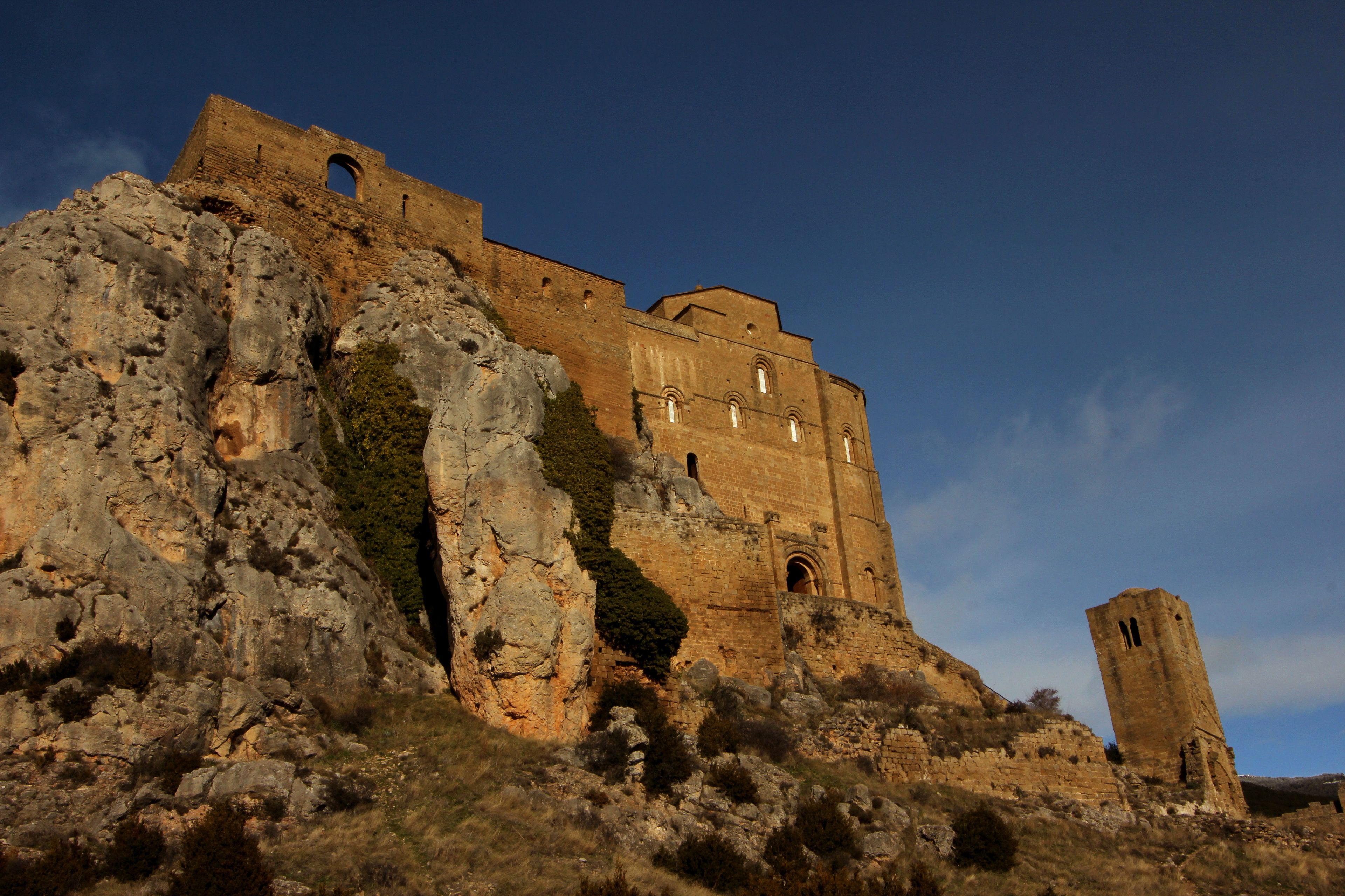 Una fortaleza de piedra histórica con una torre destacada, ubicada en una colina rocosa.