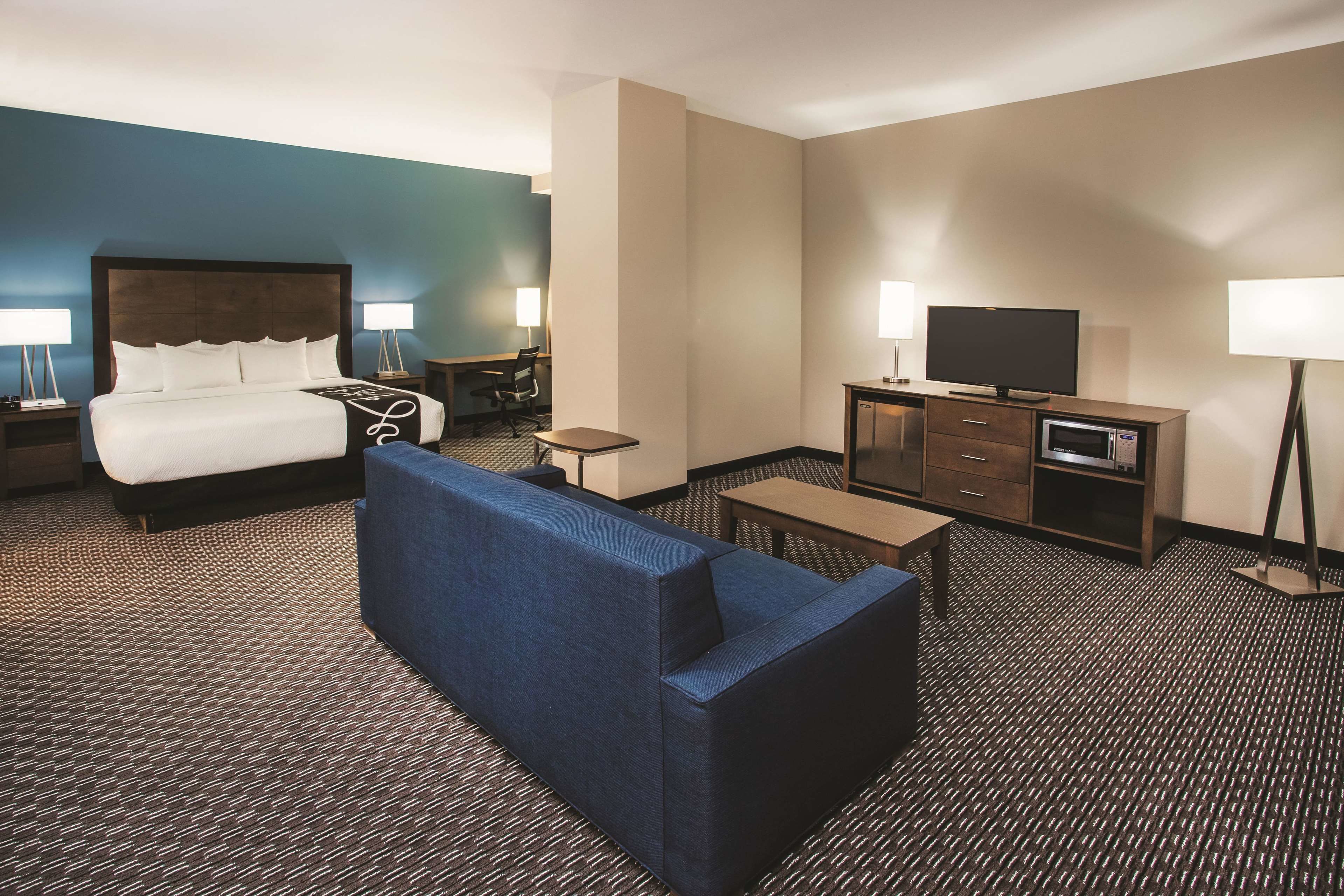 A hotel room with a bed, a blue sofa, a desk, a television, and a minibar.