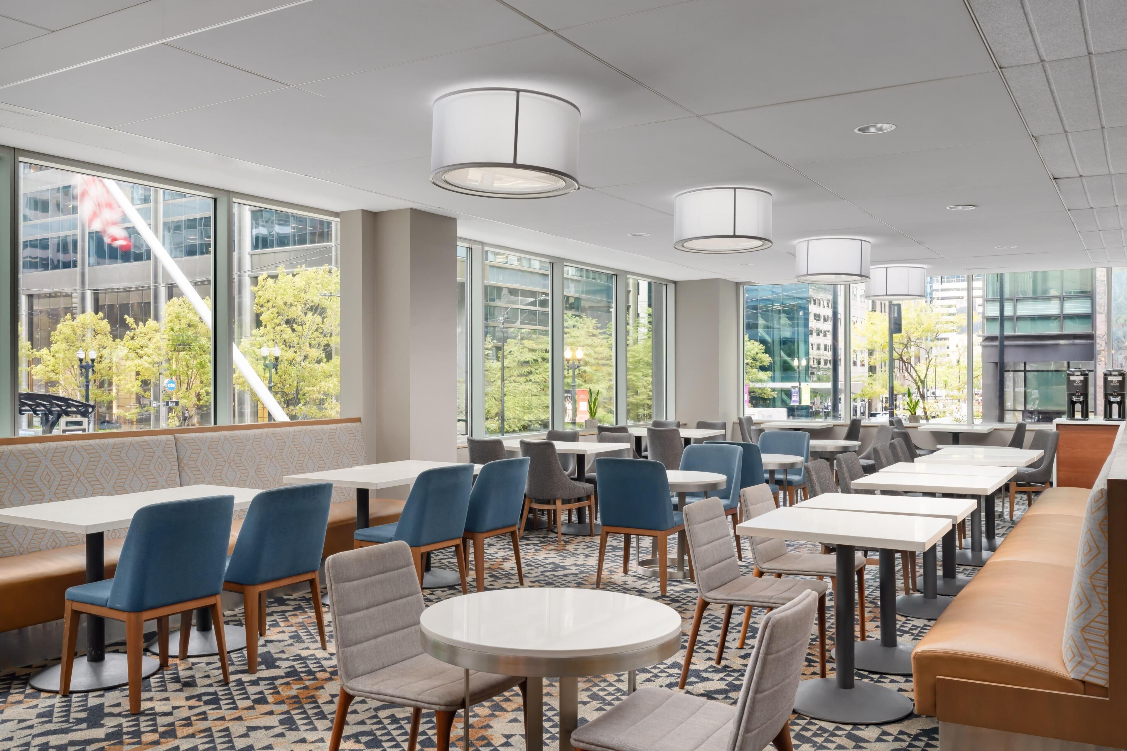 Un comedor interior moderno con amplios ventanales, diversas opciones de asientos como mesas y cabinas, y un piso con diseño.