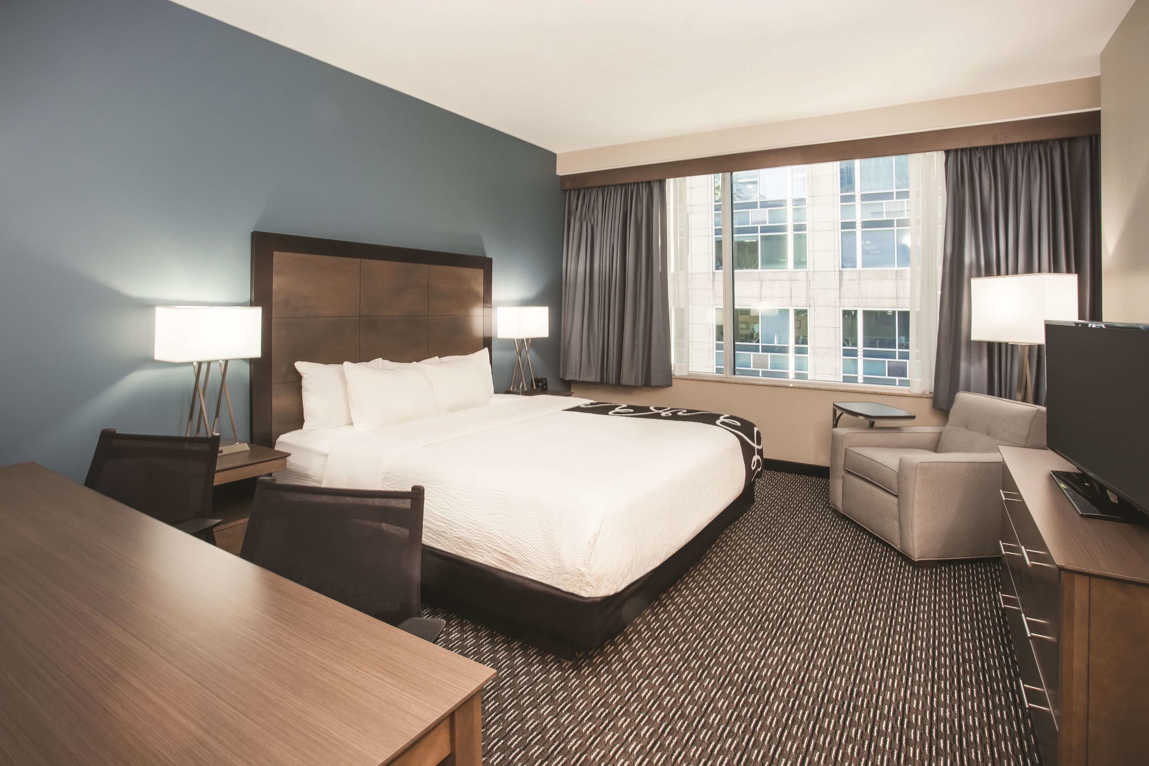 A hotel room with a large bed, a desk, a chair, a TV, and a window with curtains.