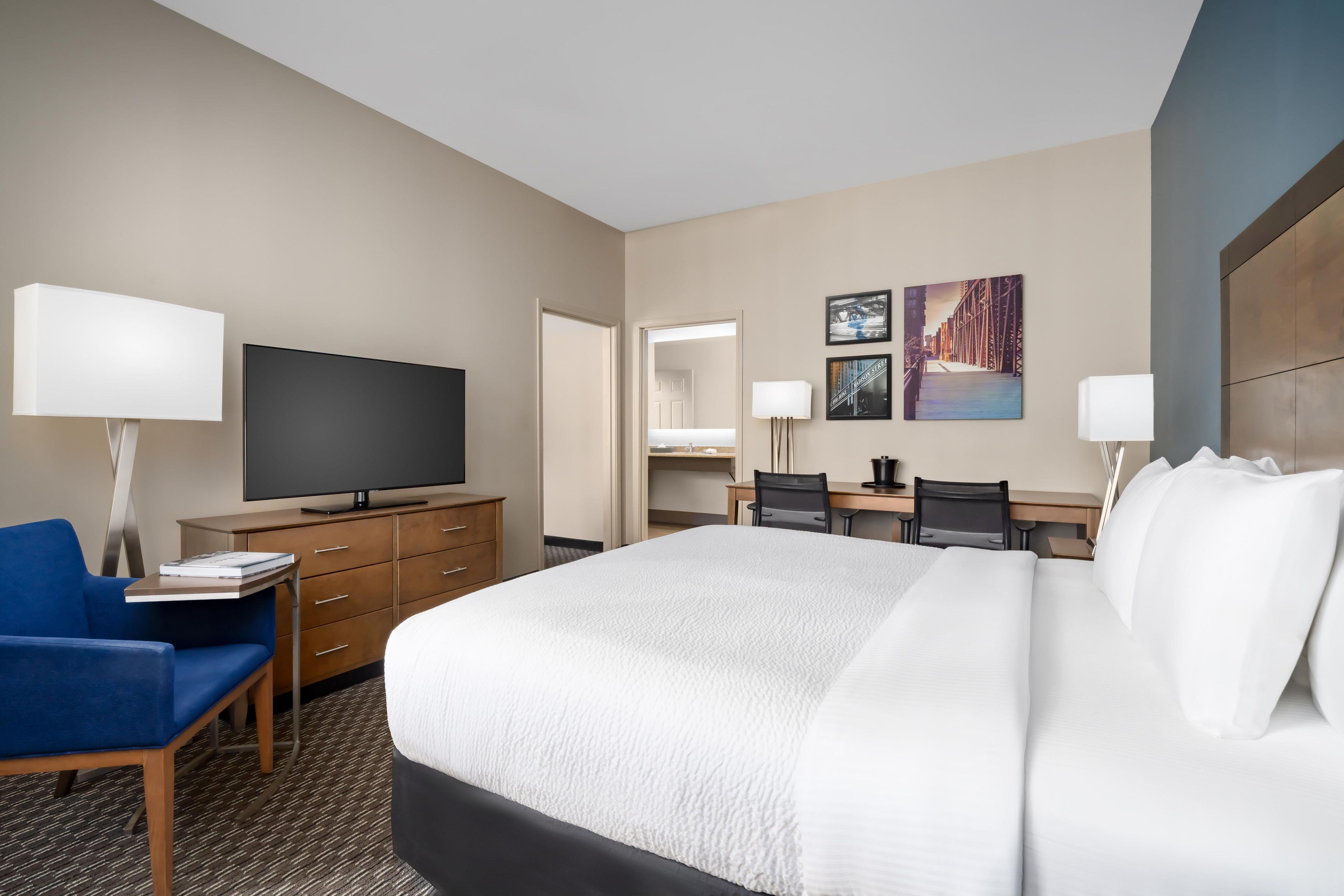 A hotel room with a large bed, a desk, a television, and a chair.