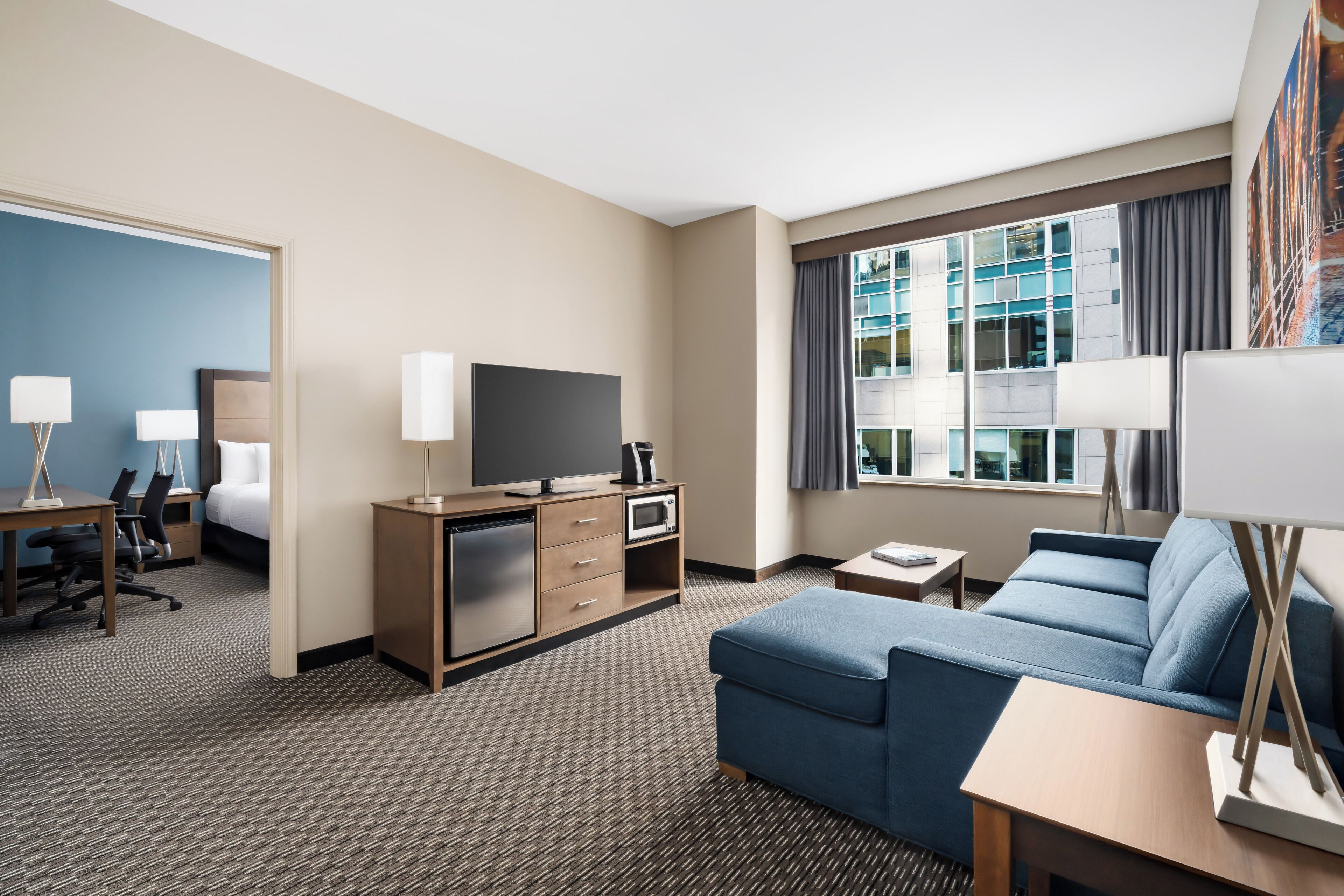 A hotel room with a bed, desk, TV, and a sofa.