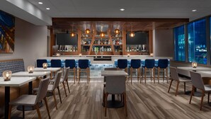 A modern bar area with a central counter, multiple seating tables, and a large window offering a view. - La Quinta Inn & Suites by Wyndham Chicago Downtown (Chicago)