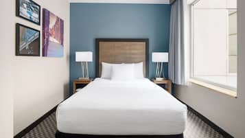 A hotel room with a large bed, two bedside tables with lamps, a window with curtains, and three framed pictures on the wall.