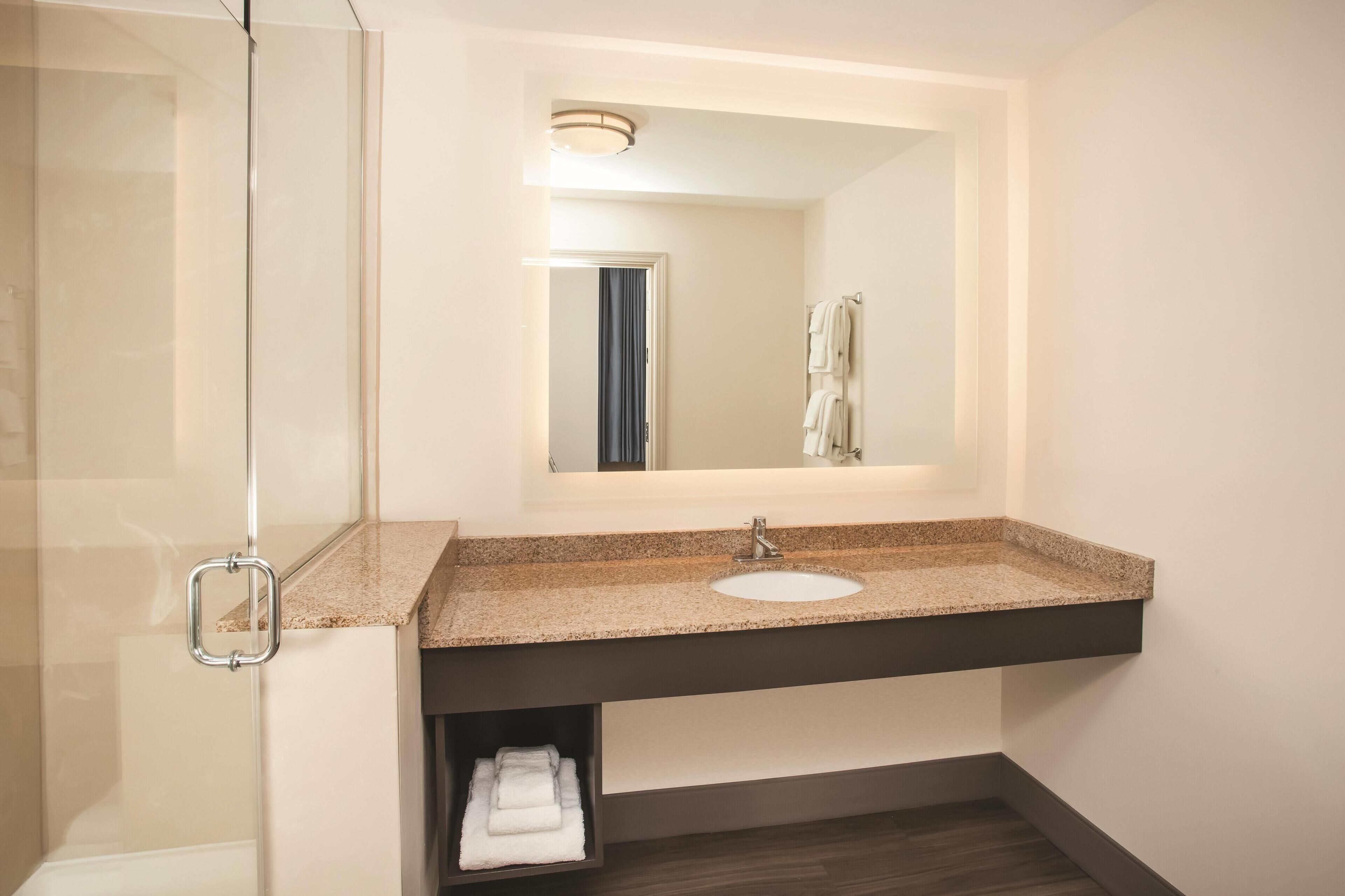 Une salle de bain moderne dotée d’une douche à parois de verre, d’un lavabo surmonté d’un plan de travail en granit et d’un porte-serviettes intégré.
