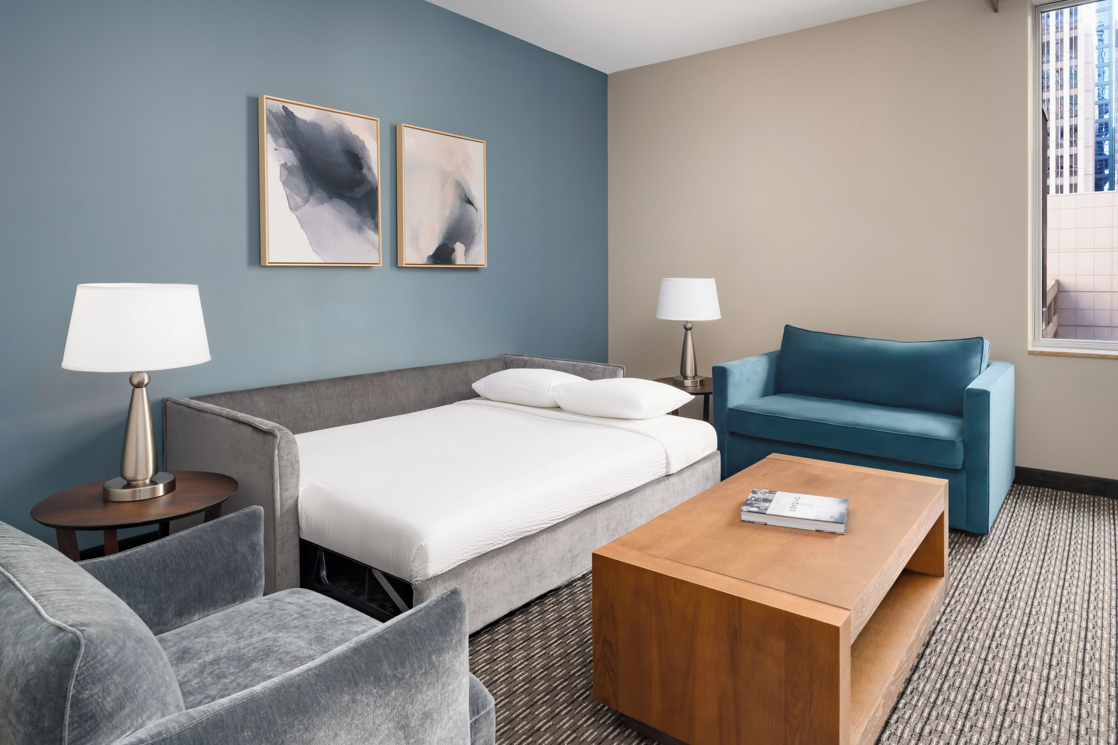 Quarto de hotel com cama, sofá, mesa de centro e duas luminárias.
