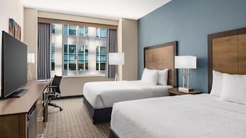A hotel room with two beds, a desk with a television, and a large window with curtains.