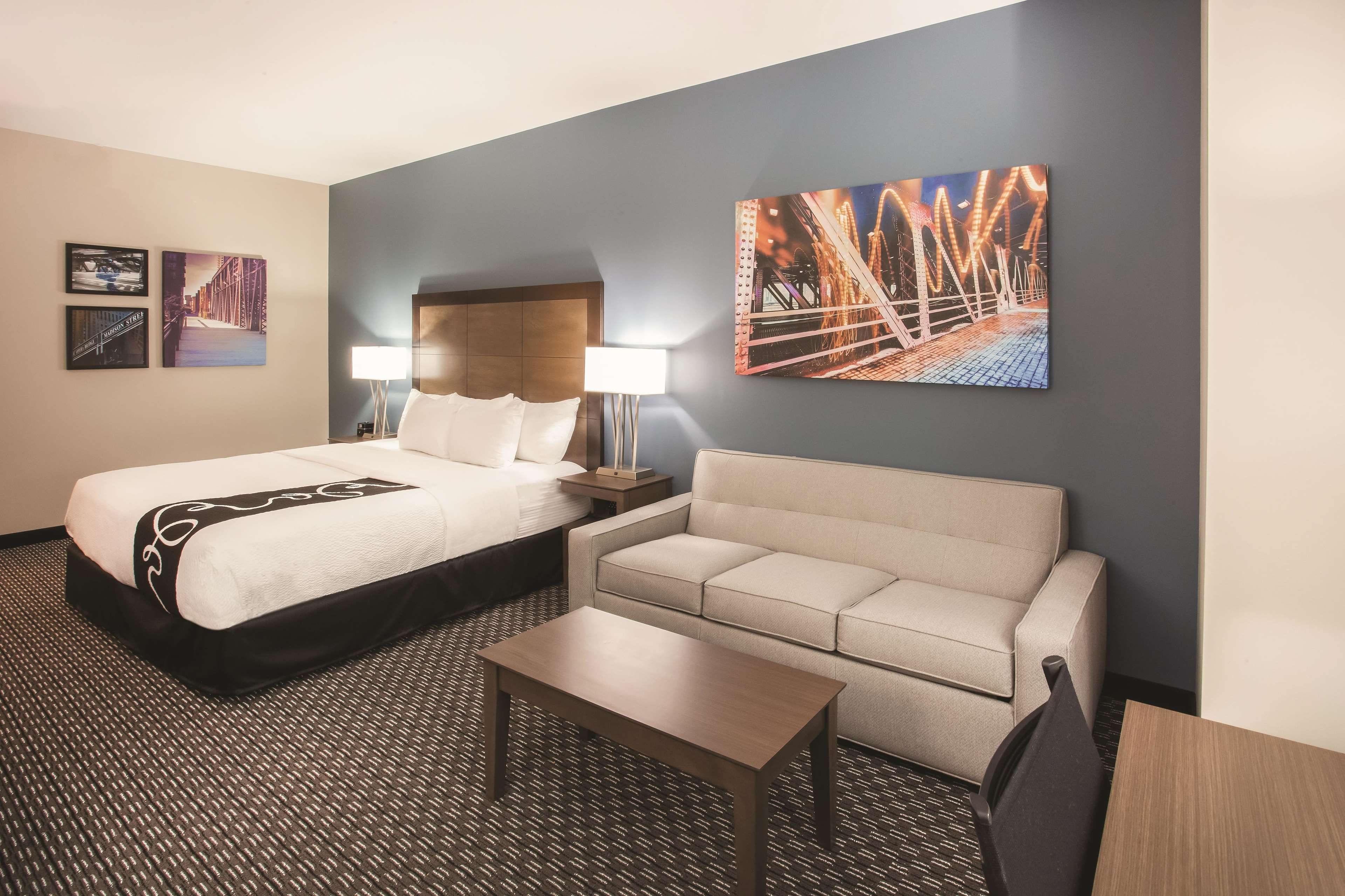 Una habitación de hotel con una cama, un sofá, una mesita y dos lámparas fijadas a la pared.