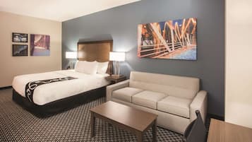 Una habitación de hotel con una cama, un sofá, una mesita y dos lámparas fijadas a la pared.