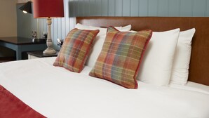 A hotel room with a bed, two plaid pillows, a red lamp, and a wooden headboard.