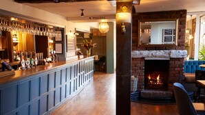 A bar area with a long counter, shelves with bottles, and a fireplace.