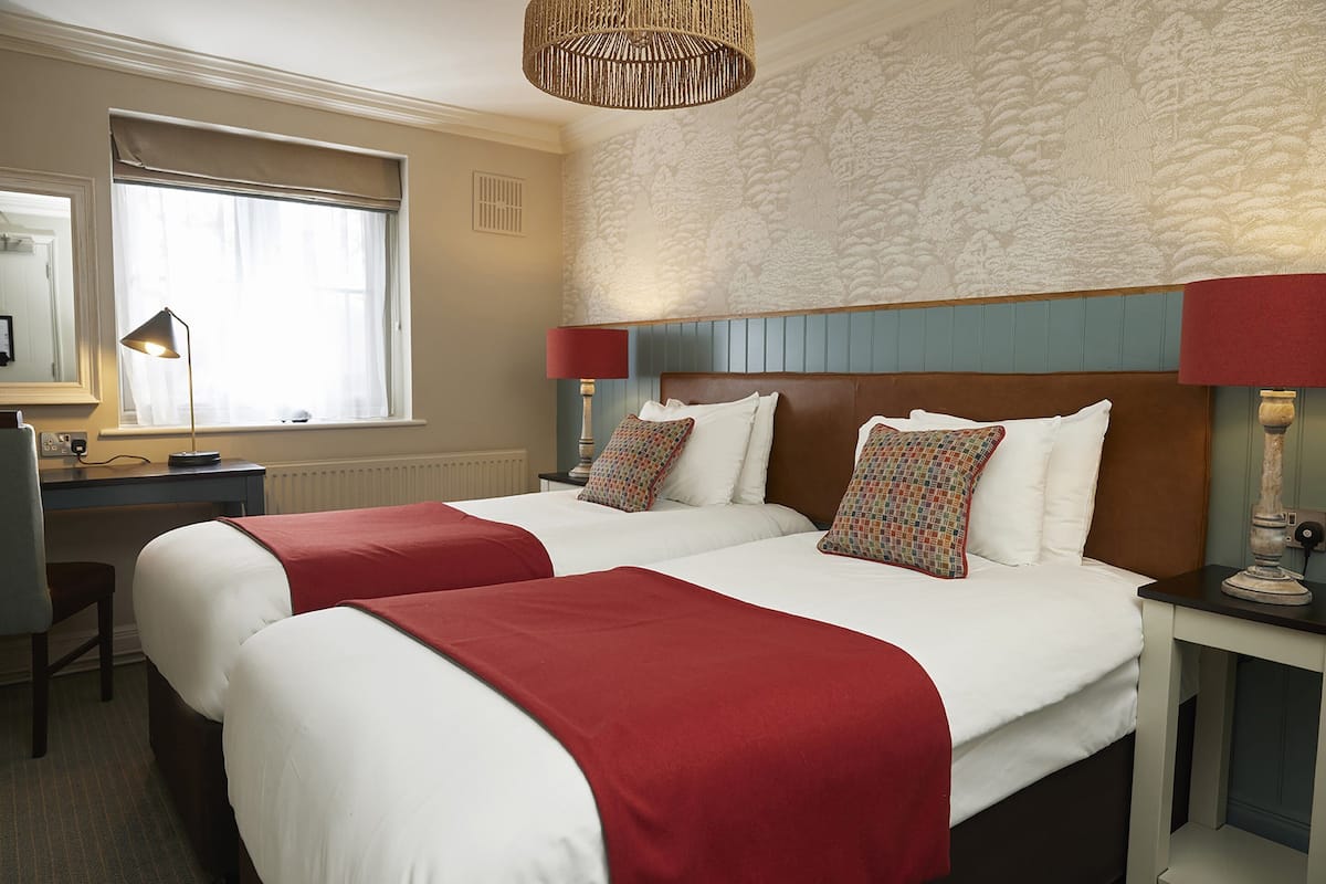 A hotel room with two beds, a desk, and a window.