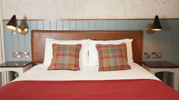 Una cama bien hecha con almohadones de cuadros, un cabecero de madera y dos lámparas fijadas a la pared.