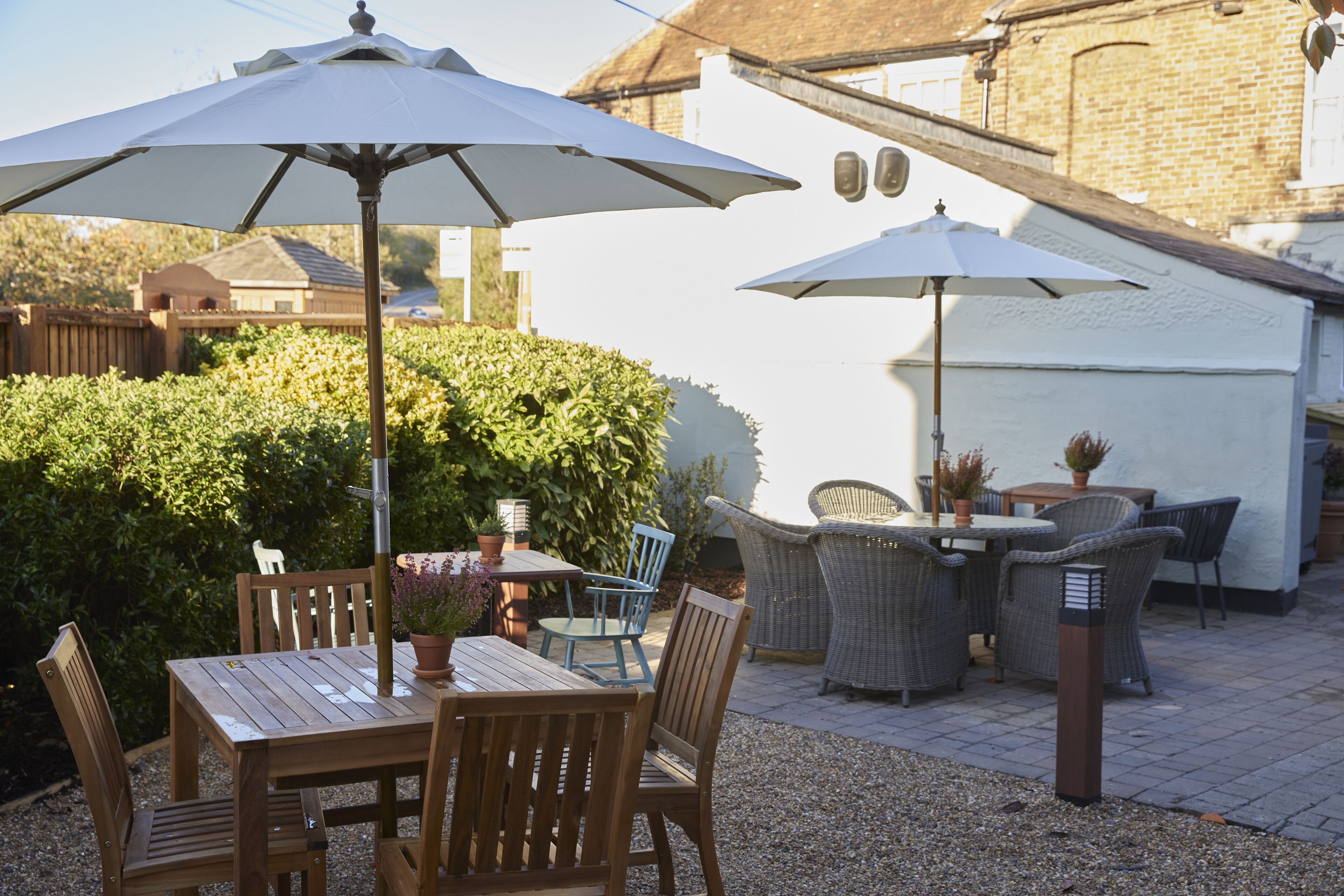 An outdoor patio with wooden tables and chairs, white umbrellas, and wicker furniture.