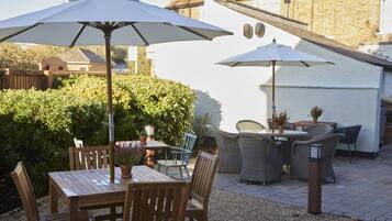 An outdoor patio with wooden tables and chairs, white umbrellas, and wicker furniture.