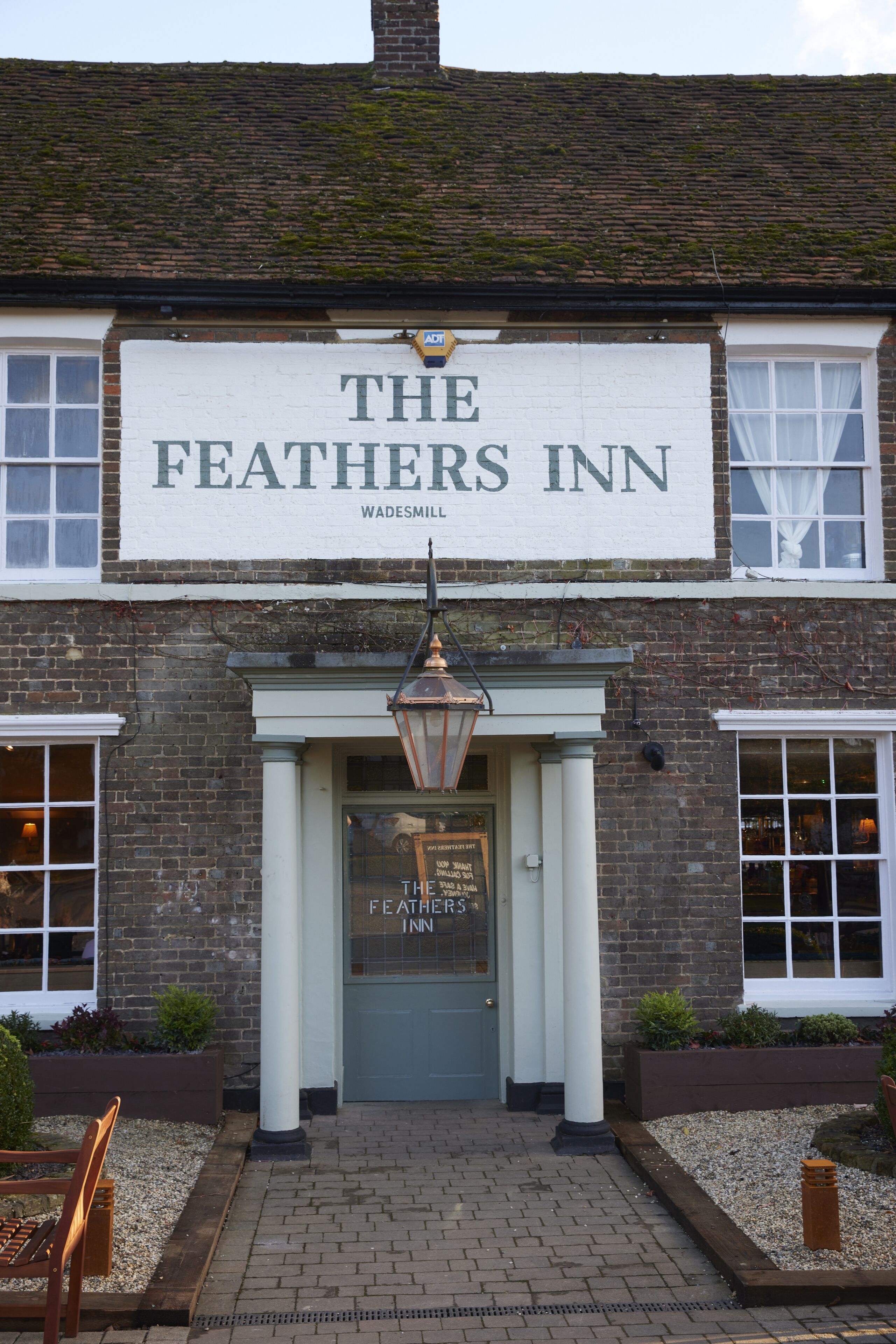 The exterior of The Feather's Inn, featuring a prominent sign, a traditional entrance with a lantern, and a brick facade.