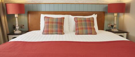 A neatly made bed with a red bedspread, two plaid pillows, and two bedside lamps with red shades.