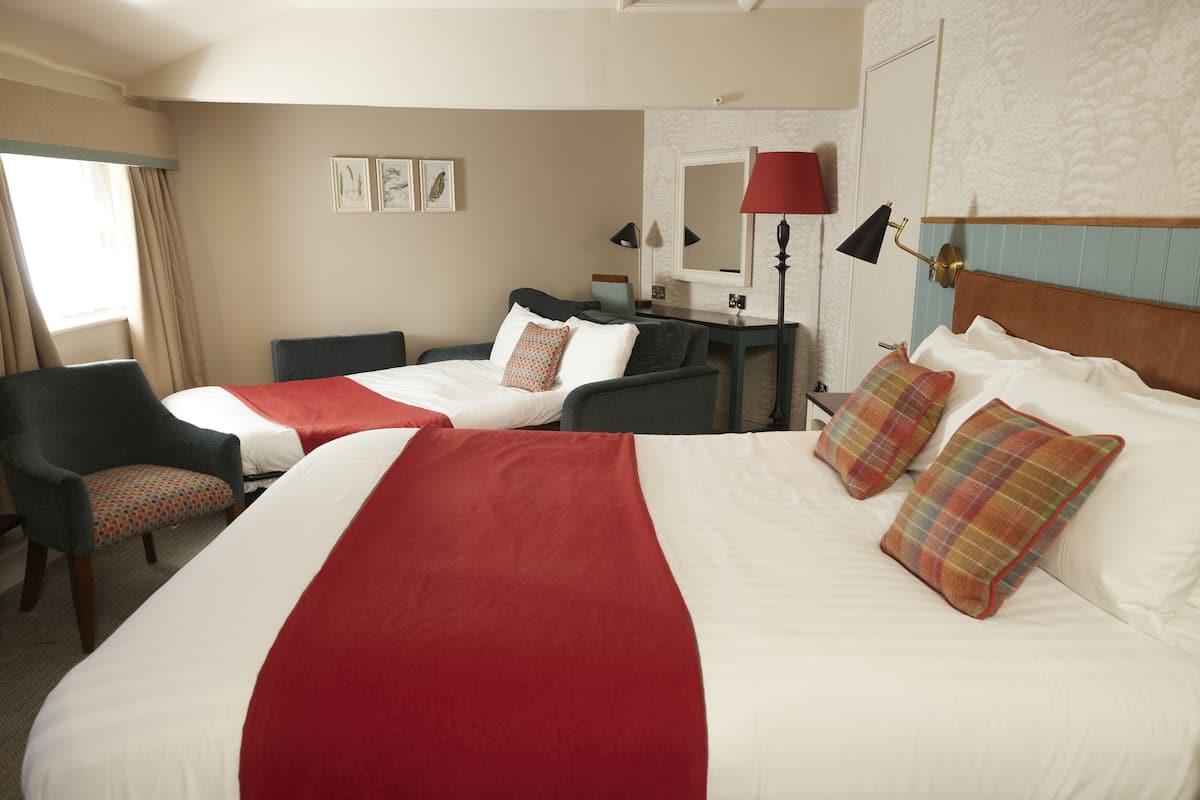 A hotel room with two beds, a desk, a chair, and a large window with curtains.