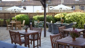 An outdoor patio area with wooden tables and chairs, two umbrellas, and a blue sofa.