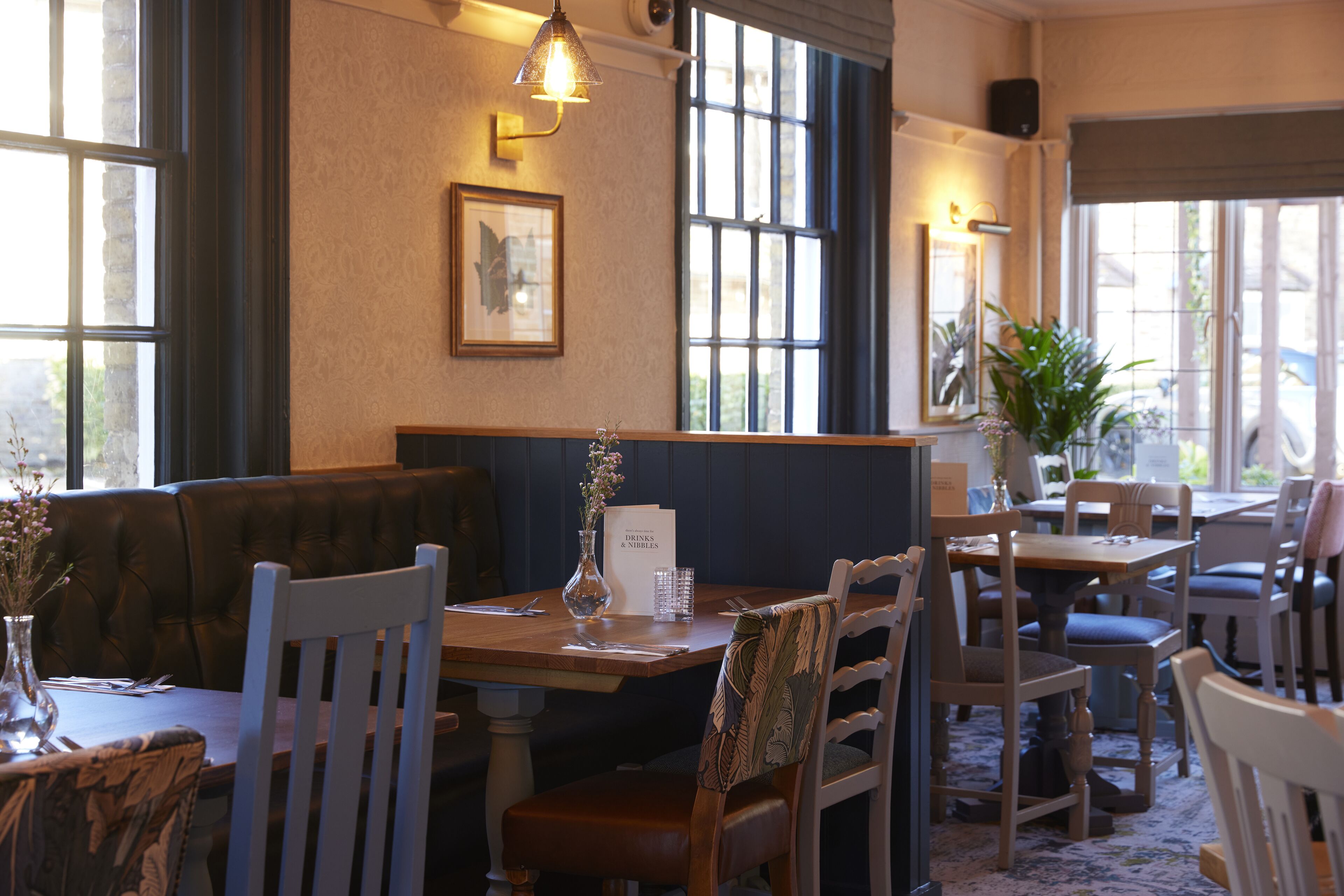 Un interior de restaurante con una mesa de madera, sillas, un banco y un jarrón con flores.