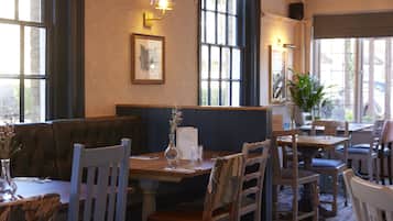 Un interior de restaurante con una mesa de madera, sillas, un banco y un jarrón con flores.