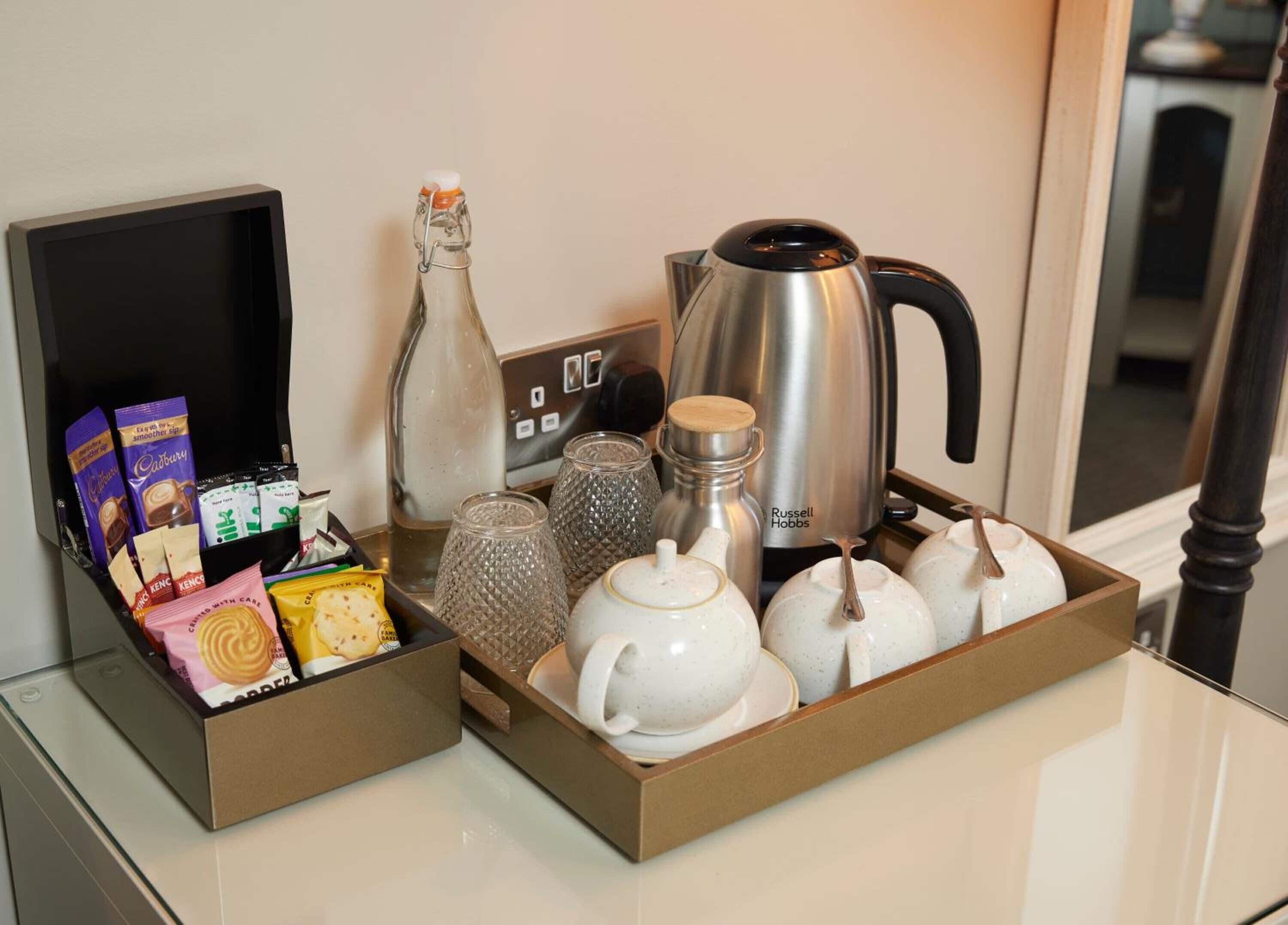 A breakfast tray with assorted snacks, a bottle, a kettle, and teapots.