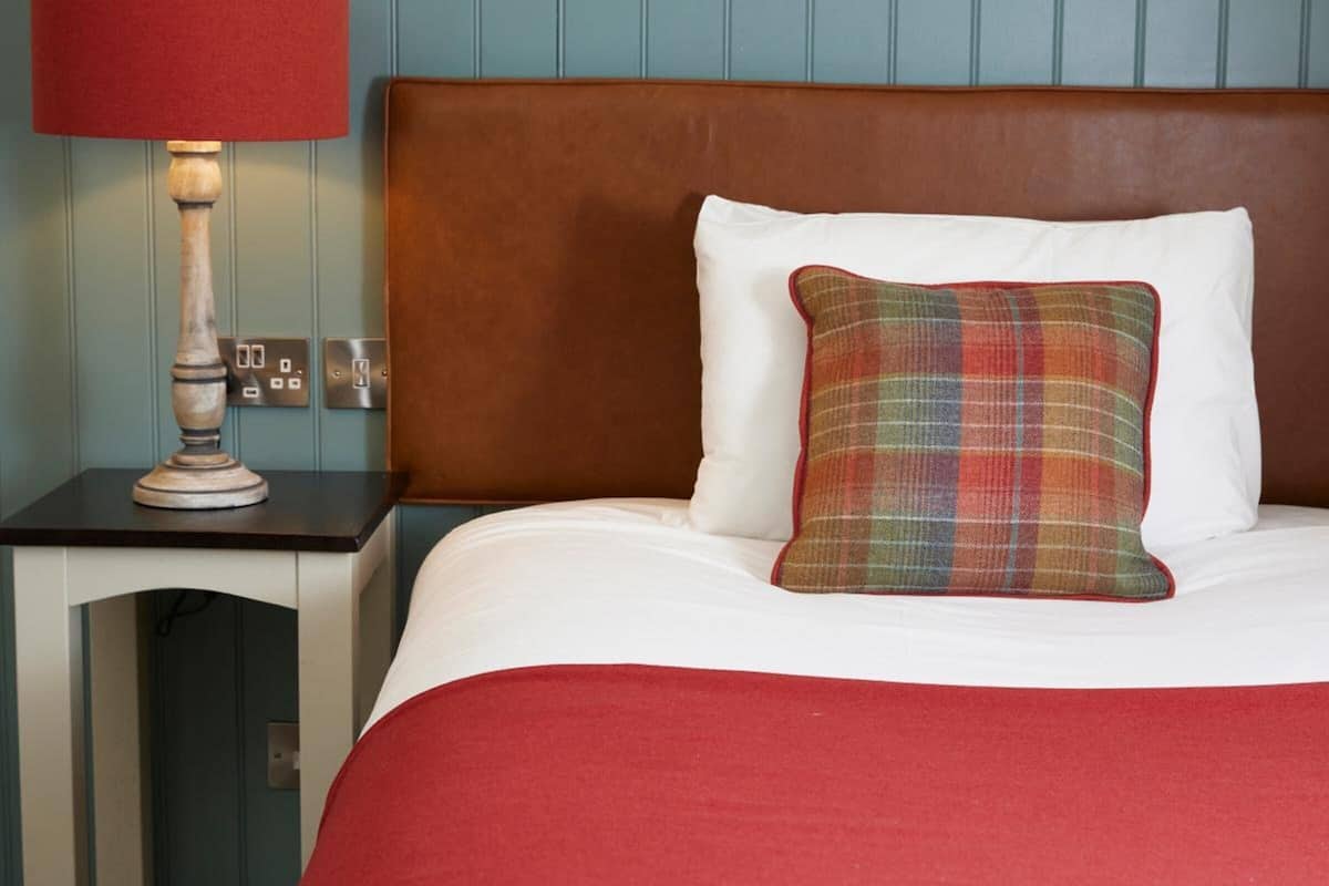 A hotel room with a bed, a nightstand, a lamp, and a headboard.