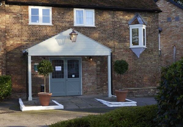 A brick building with a white entrance, two potted plants, and a small window.