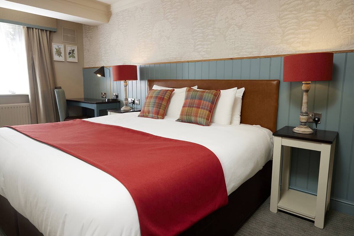A hotel room with a large bed, two bedside lamps, a desk, and a chair.