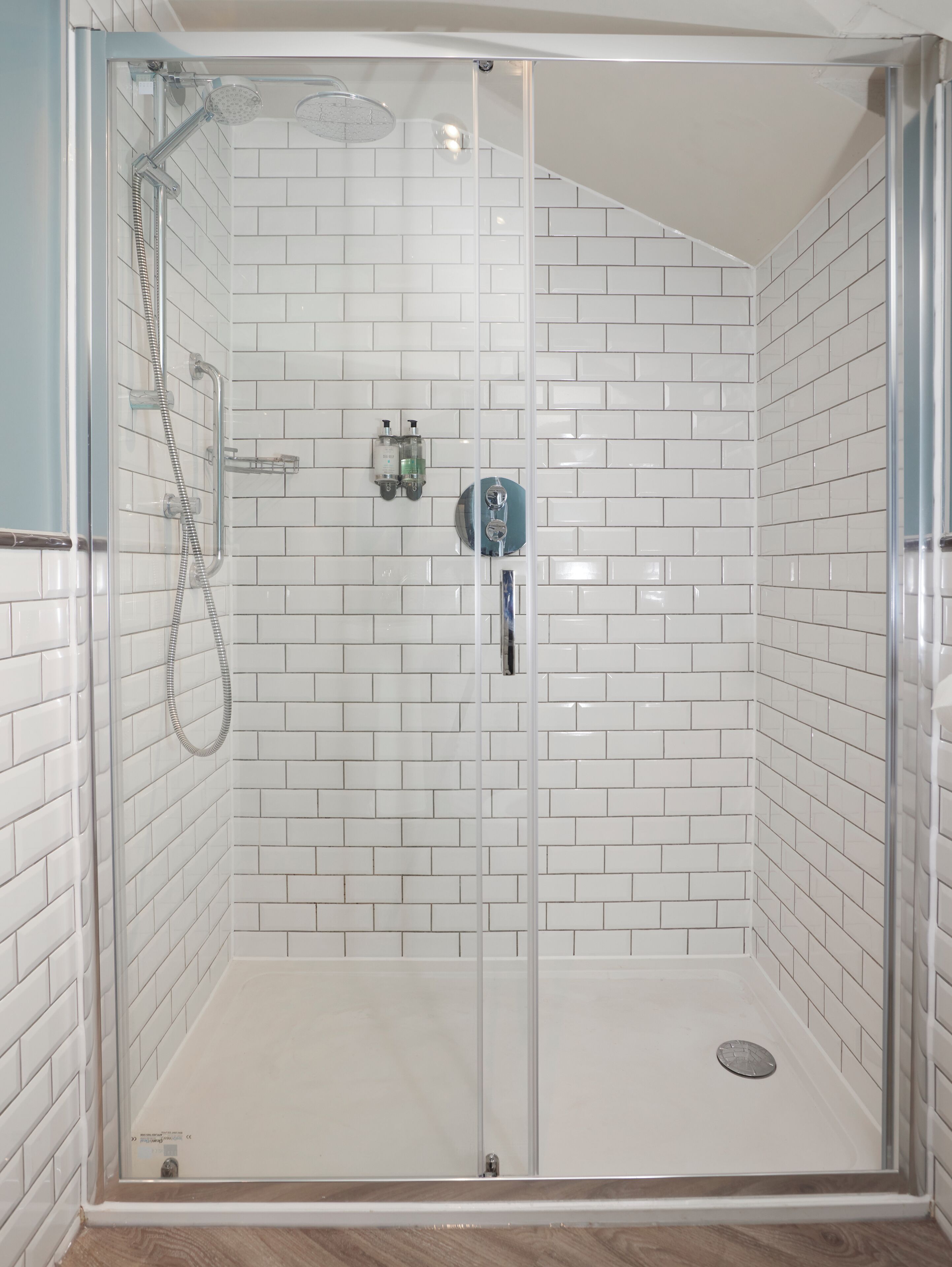 Une douche entièrementClose avec des murs recouverts de carreaux blancs et un sol transparent.