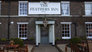 The exterior of The Feathers Inn, featuring a prominent sign, a traditional entrance with a lantern, and outdoor seating area.