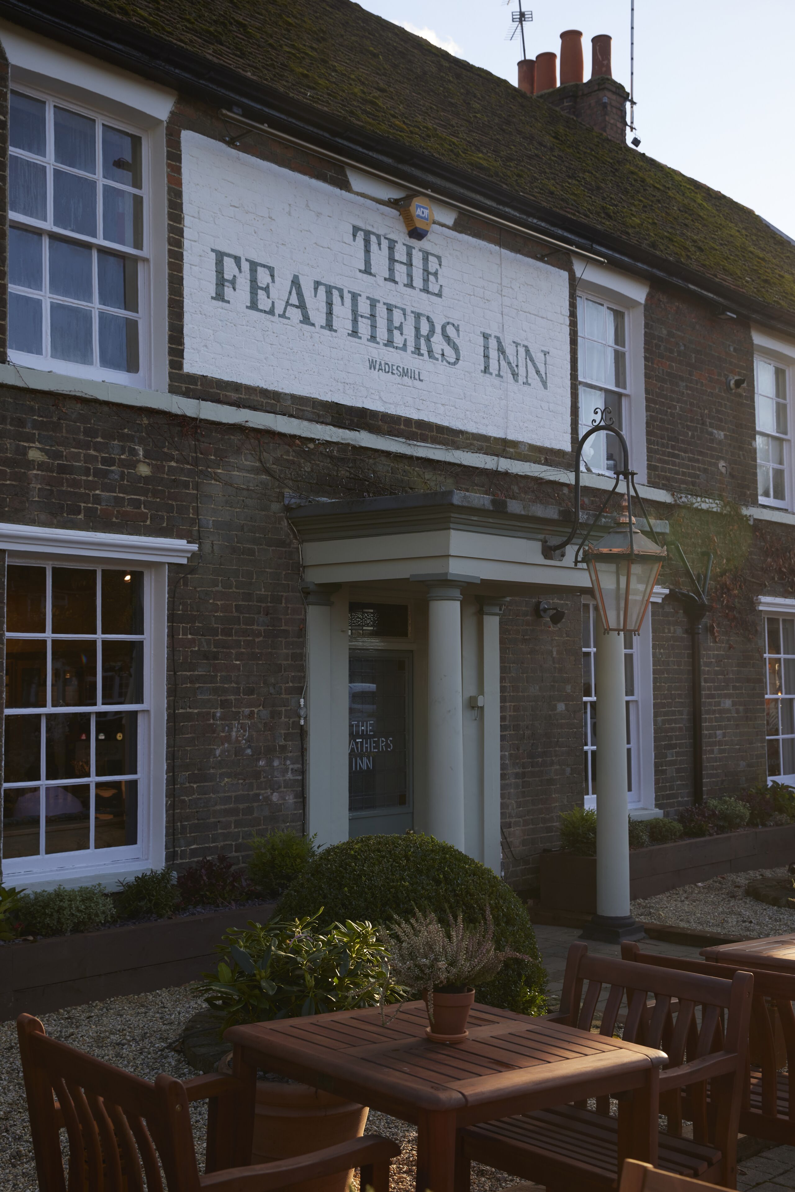 El Feathers Inn, un edificio de ladrillo tradicional con letrero, zona de asientos al aire libre y farola.