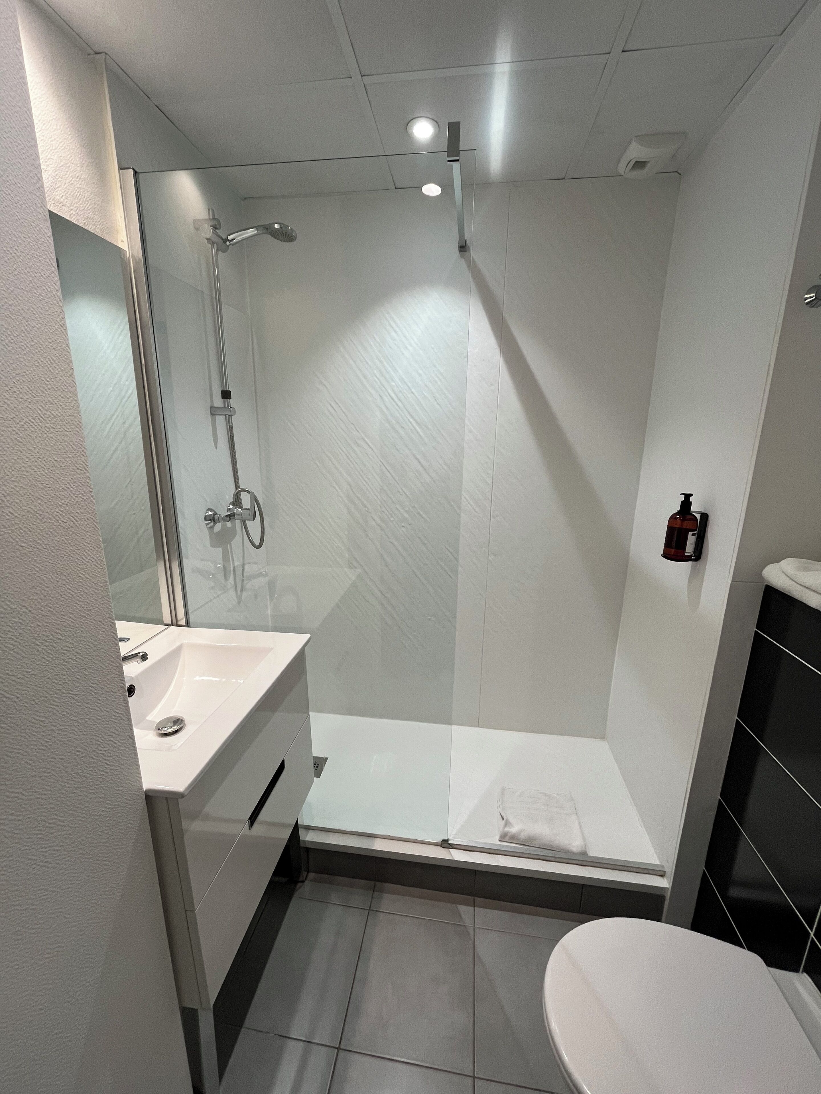 Un baño moderno con cabina de ducha de vidrio, un lavamanos blanco y un inodoro.